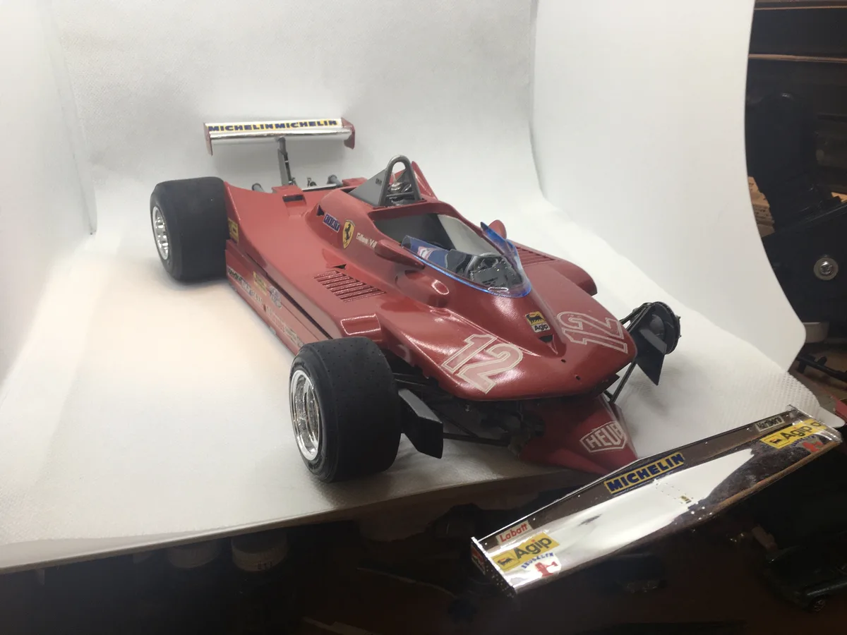 A red scale model of a vintage Ferrari Formula 1 race car, number 12, with Michelin and Agip sponsor decals, is displayed on…