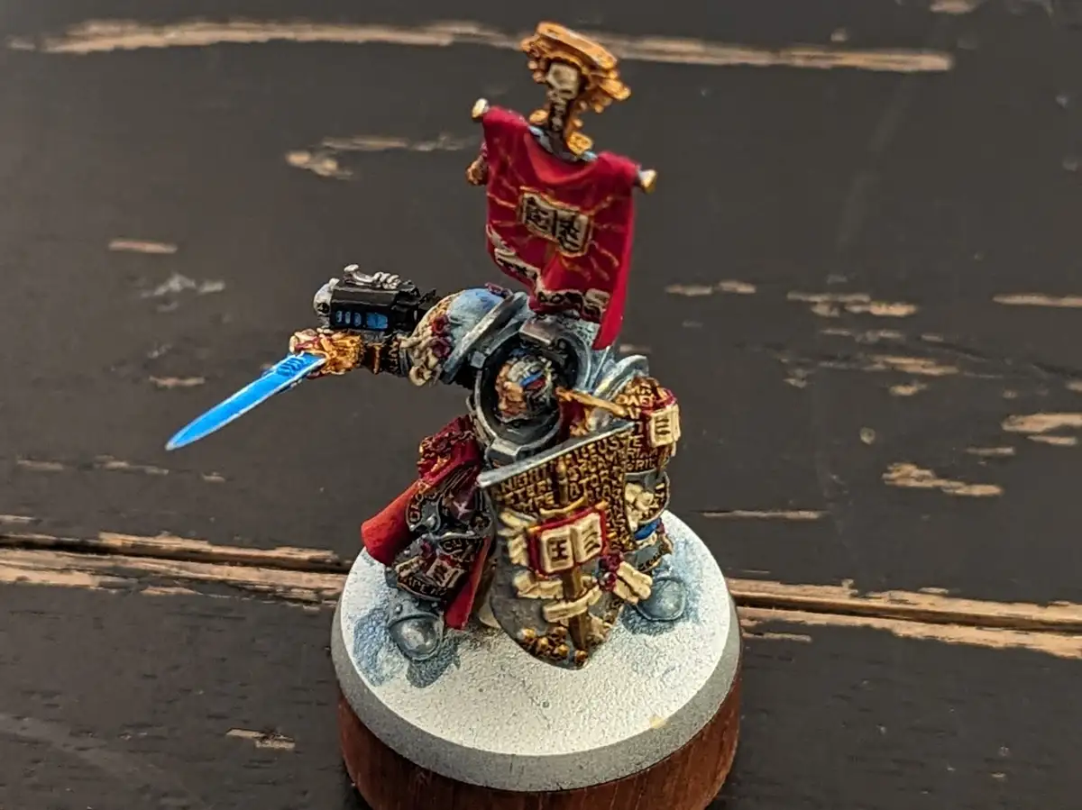 A heavily detailed, hand-painted miniature of a Space Marine from Warhammer 40,000, wearing ornate armor with red and gold…