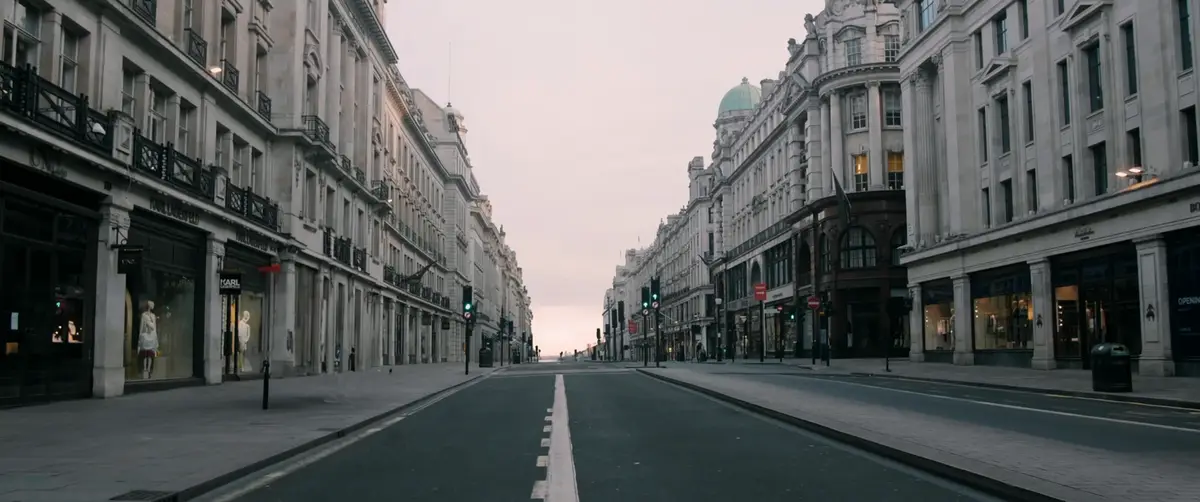 An empty, wide city street lined with ornate, multi-story buildings featuring storefronts like Karl Lagerfeld and UNO, under…