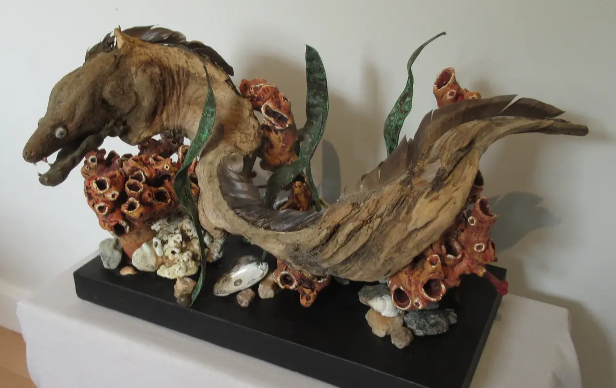 a sculpture of a horse crafted from driftwood, featuring a textured, weathered body with a horse-like head and tail…
