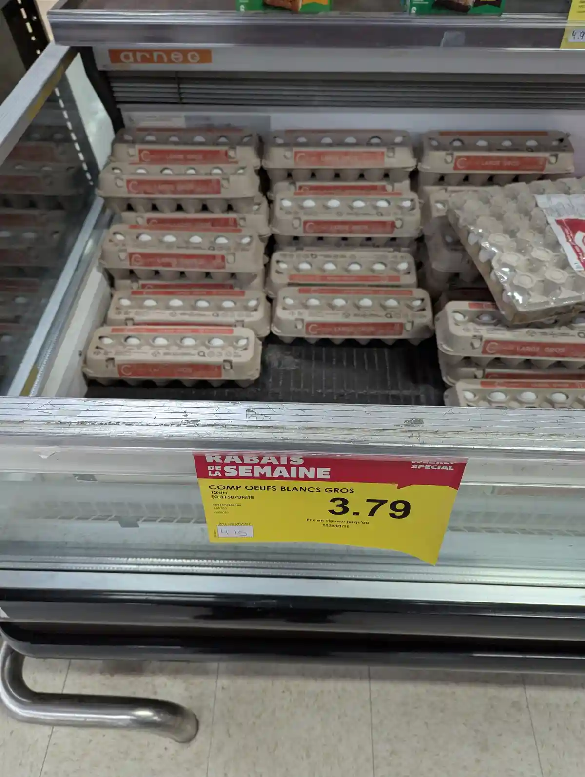 A supermarket egg refrigerated shelf displays multiple cartons of large white eggs, with a prominent yellow and red price…