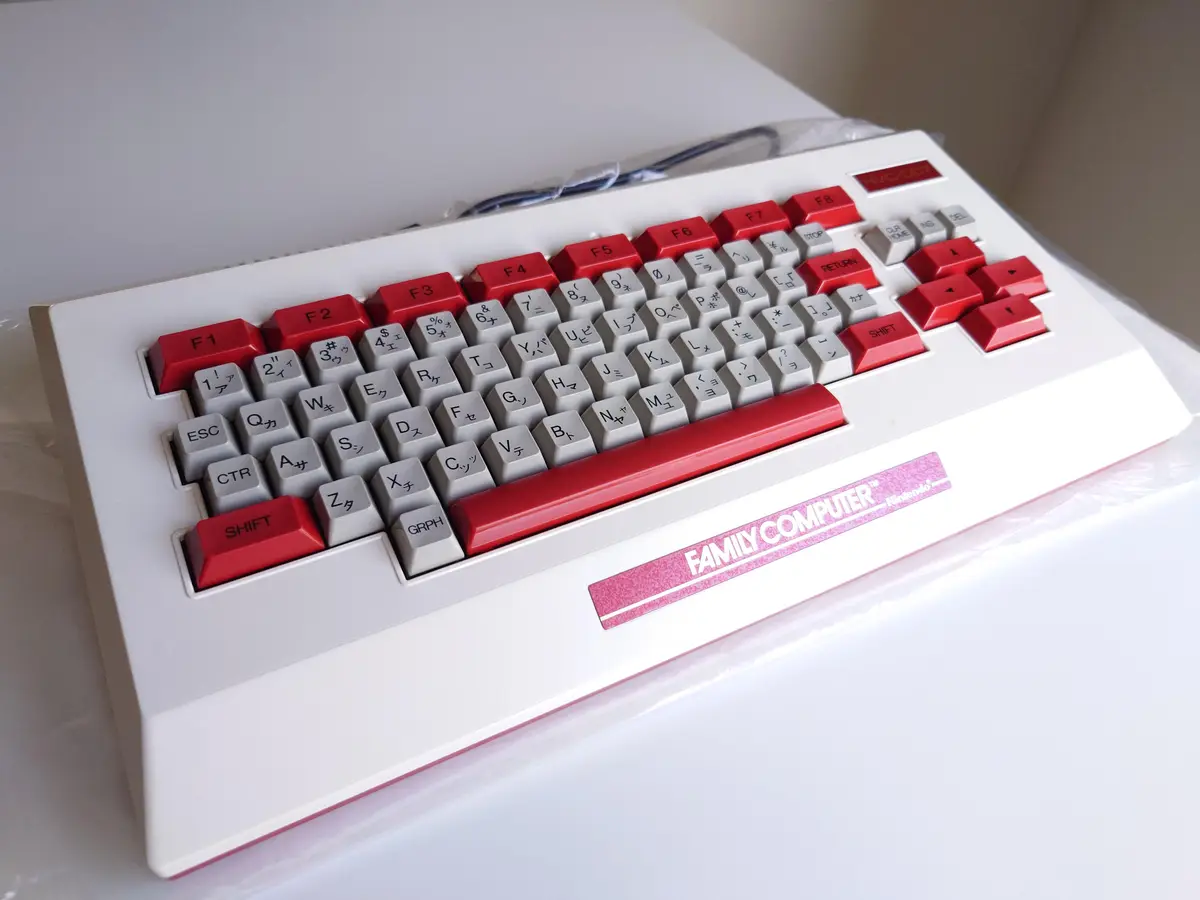 A close-up photo of a white and red Nintendo Family Computer (Famicom) keyboard, showing its distinctive layout with red…