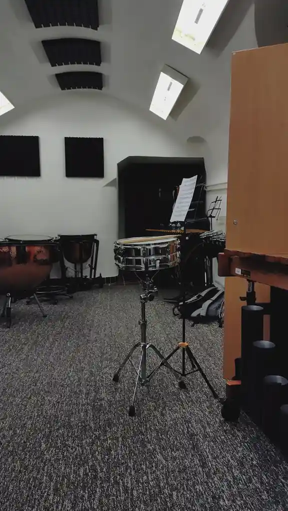 A dimly lit, empty music practice room with sound-dampening panels on the curved ceiling and walls, featuring a snare drum…