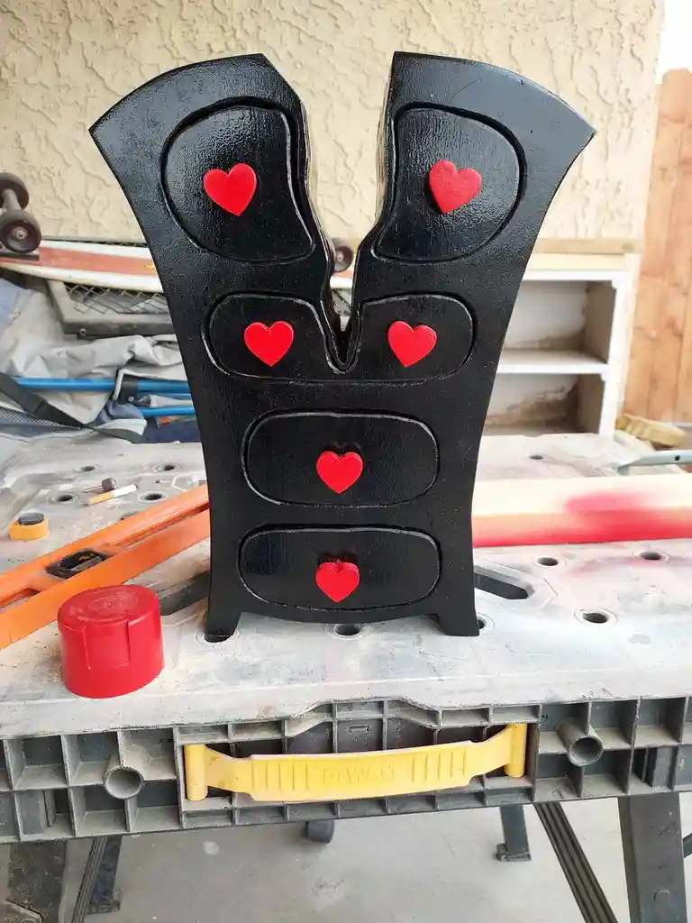 A black, heart-shaped object, resembling a tool or sculpture, is decorated with five red hearts and sits on a workbench. The…
