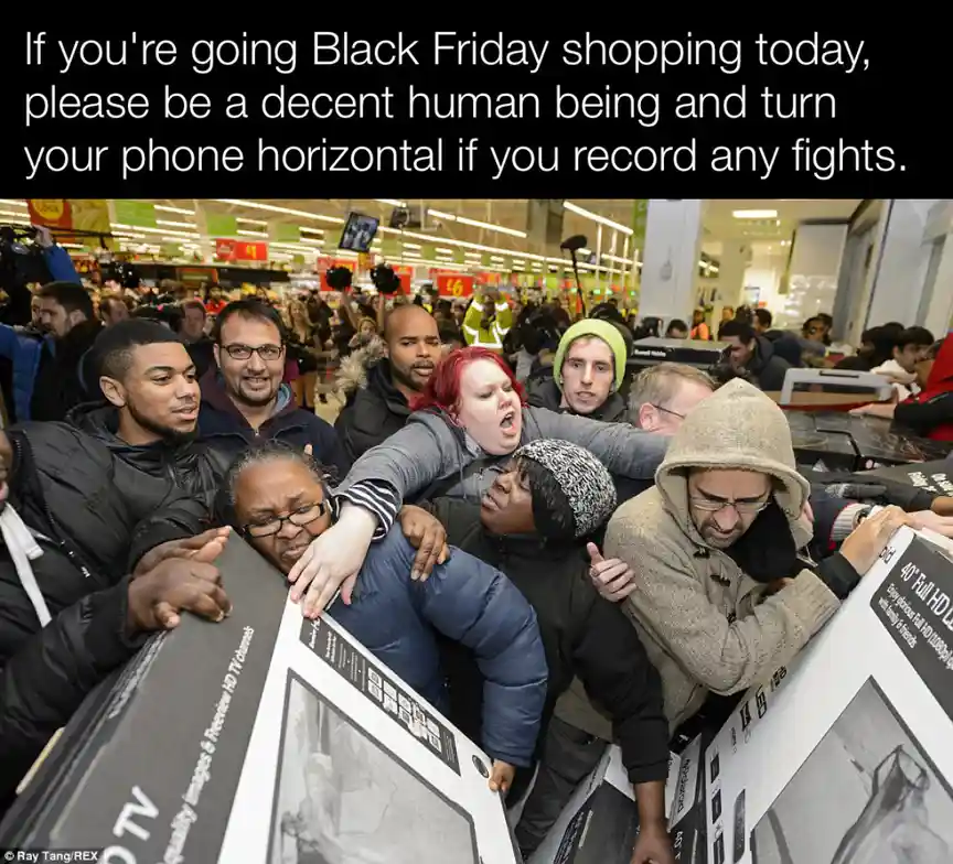 A crowded Black Friday scene shows shoppers physically struggling over large TV boxes in a store aisle. People are pushing…
