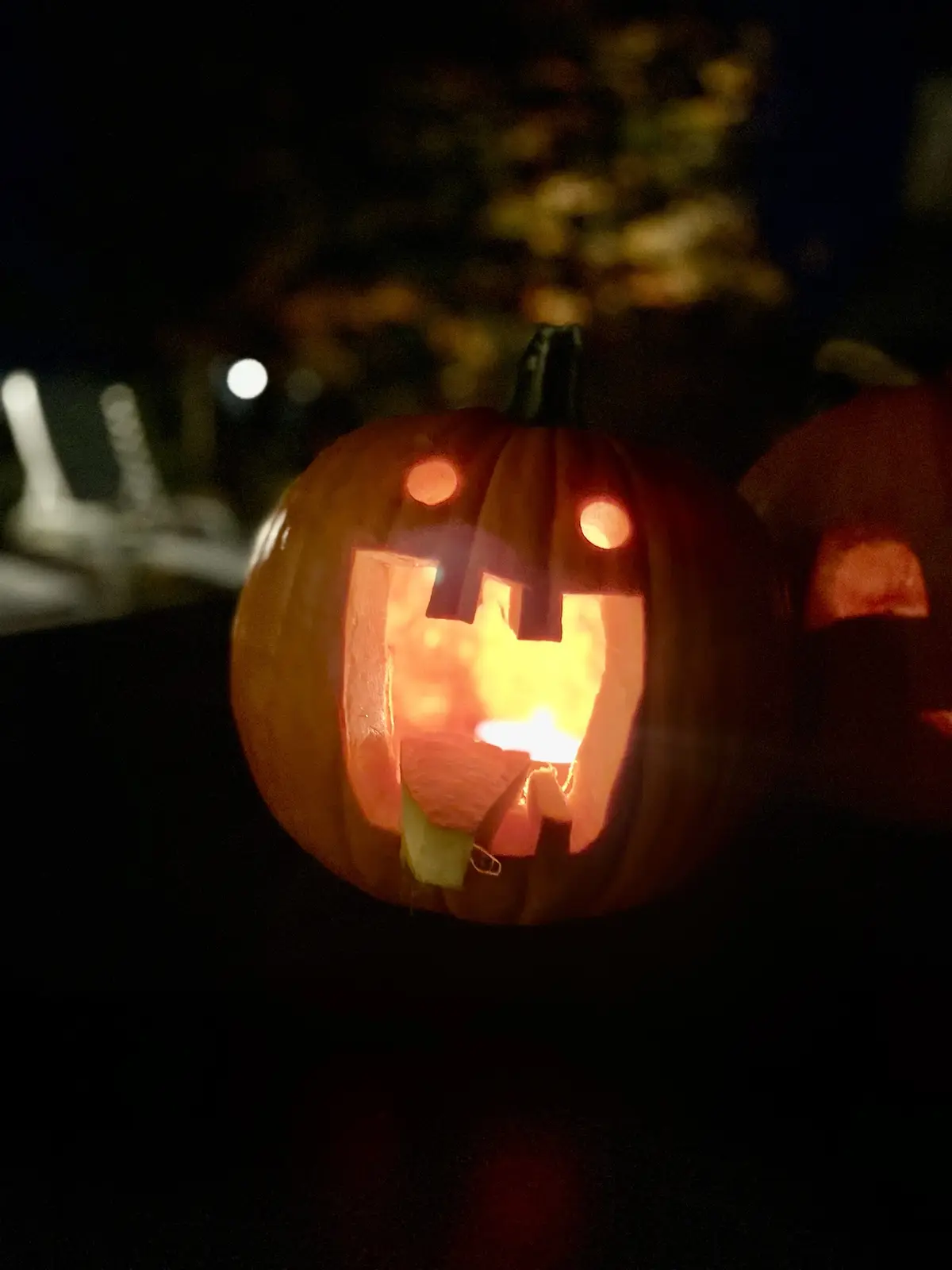 A close-up of a carved Halloween pumpkin with a lit candle inside, its face illuminated from within. The pumpkin has round…