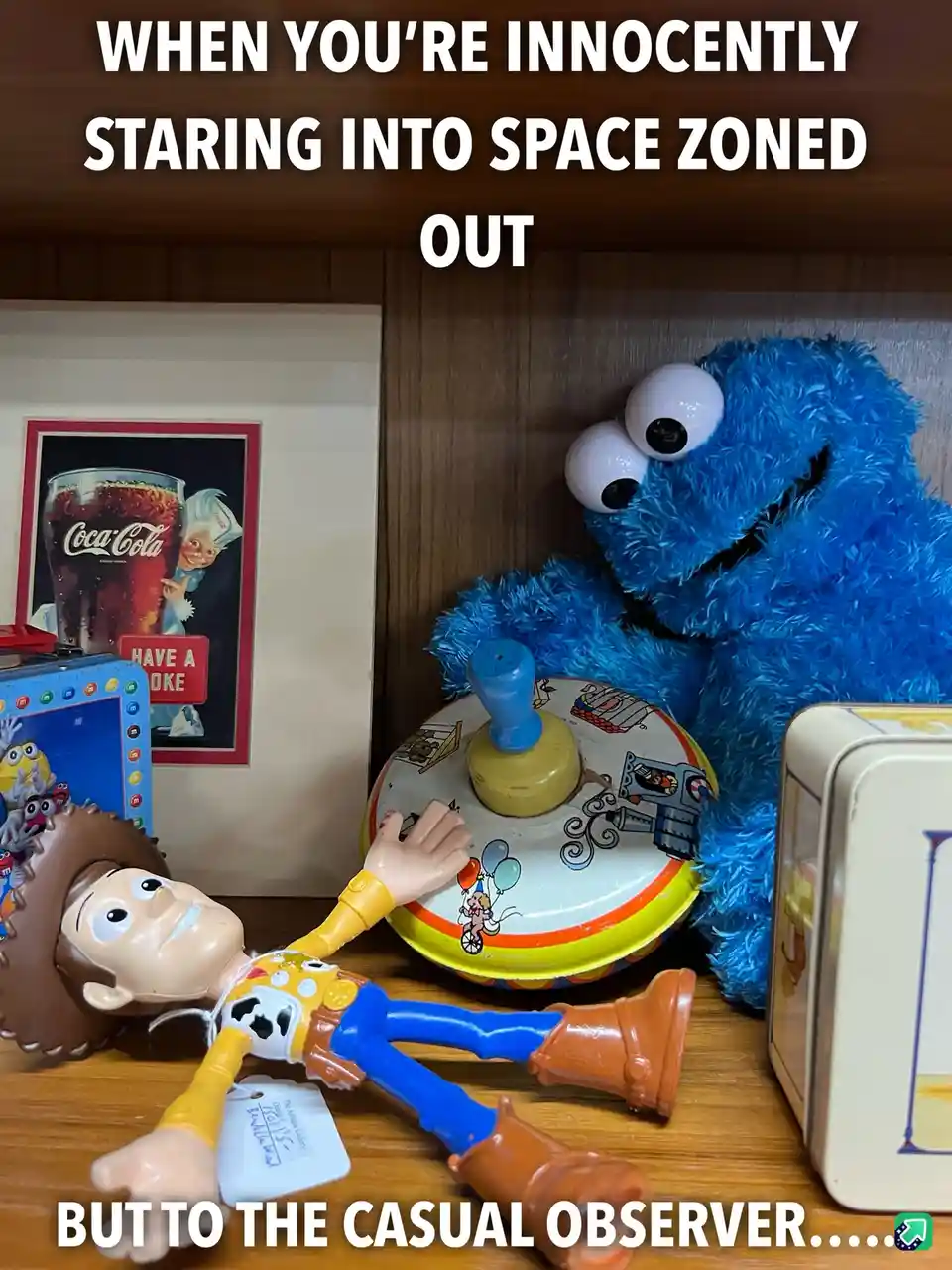 A toy Woody from Toy Story lies on his back on a wooden shelf, appearing to stare blankly upward, while a blue, furry Cookie…