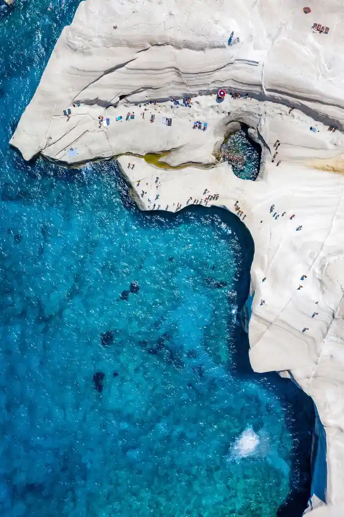 An aerial view of a stunning beach with white, layered rock formations and vibrant turquoise water, where the natural shape…