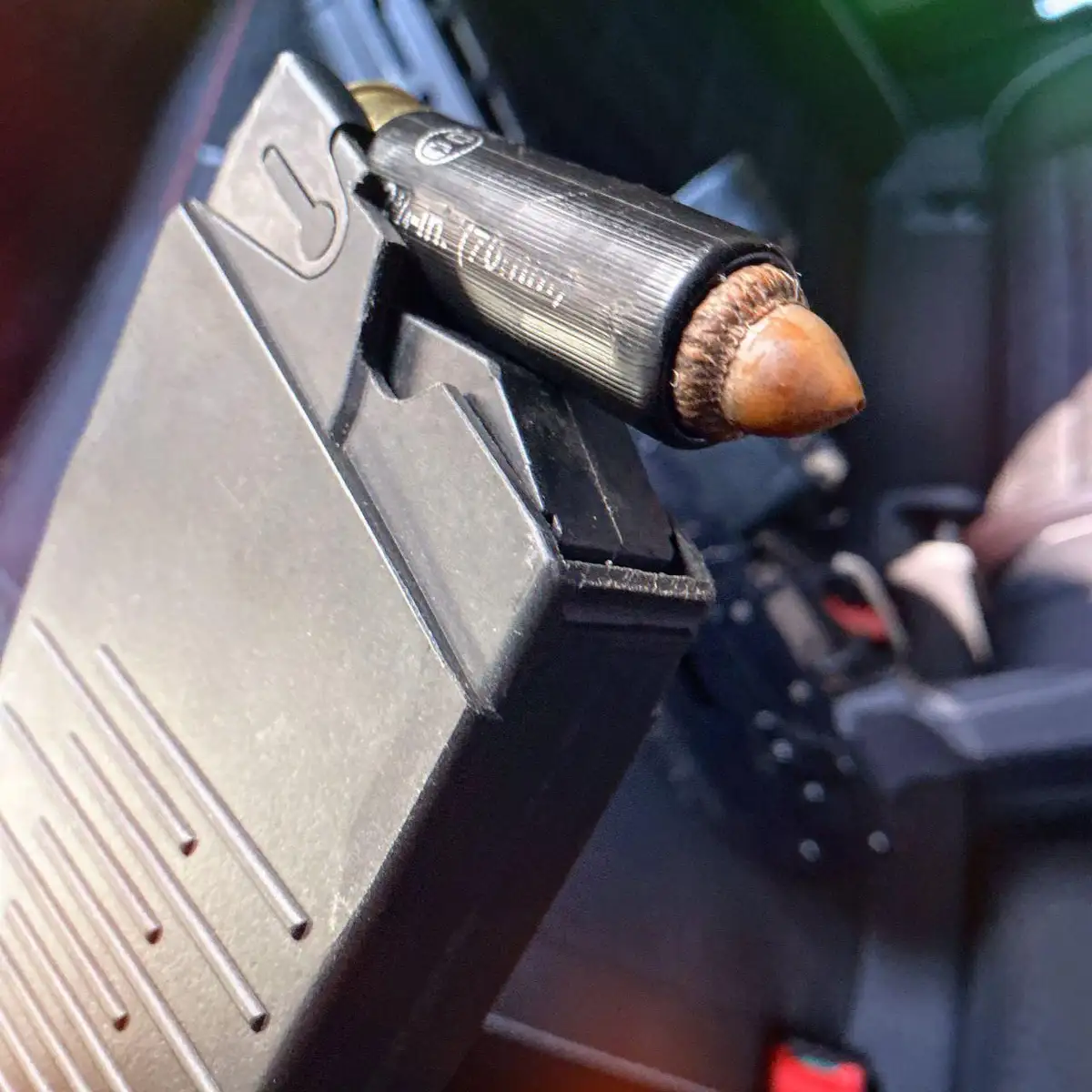 A close-up photo shows a real acorn inserted into the barrel of a firearm, appearing as if it were a bullet. The firearm's…