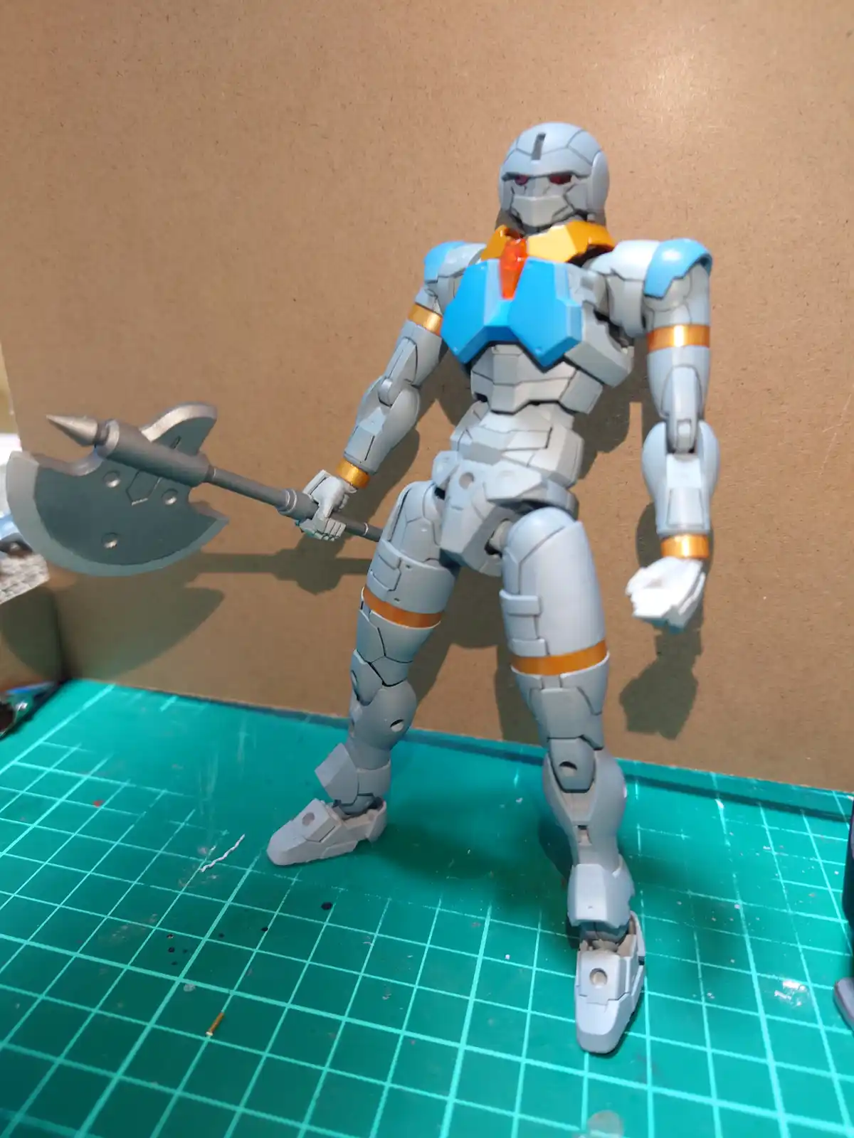 A grey and blue robot action figure with orange accents stands on a green grid mat holding a large axe, with the text 'i'm…