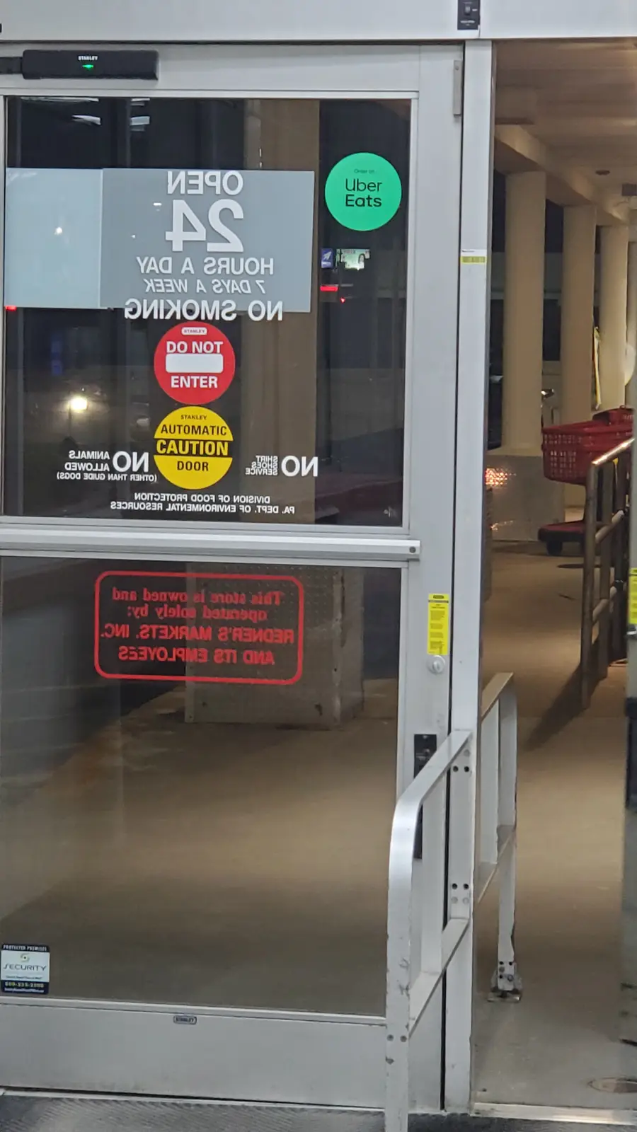 A photo of a glass store door covered in various signs including 'OPEN 24 HOURS A DAY 7 DAYS A WEEK', 'NO SMOKING', 'DO NOT…