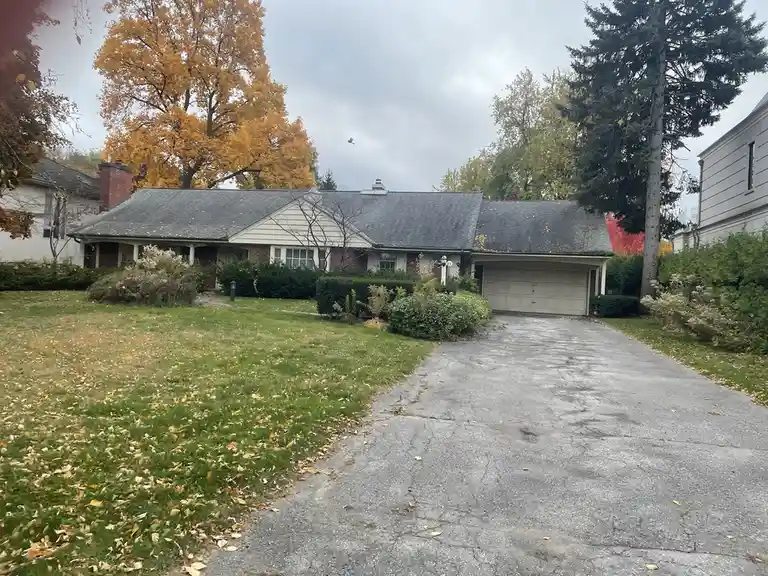 A photo of a suburban house in autumn with fallen leaves on the lawn and a cracked driveway, overlaid with the text 'i'm not…
