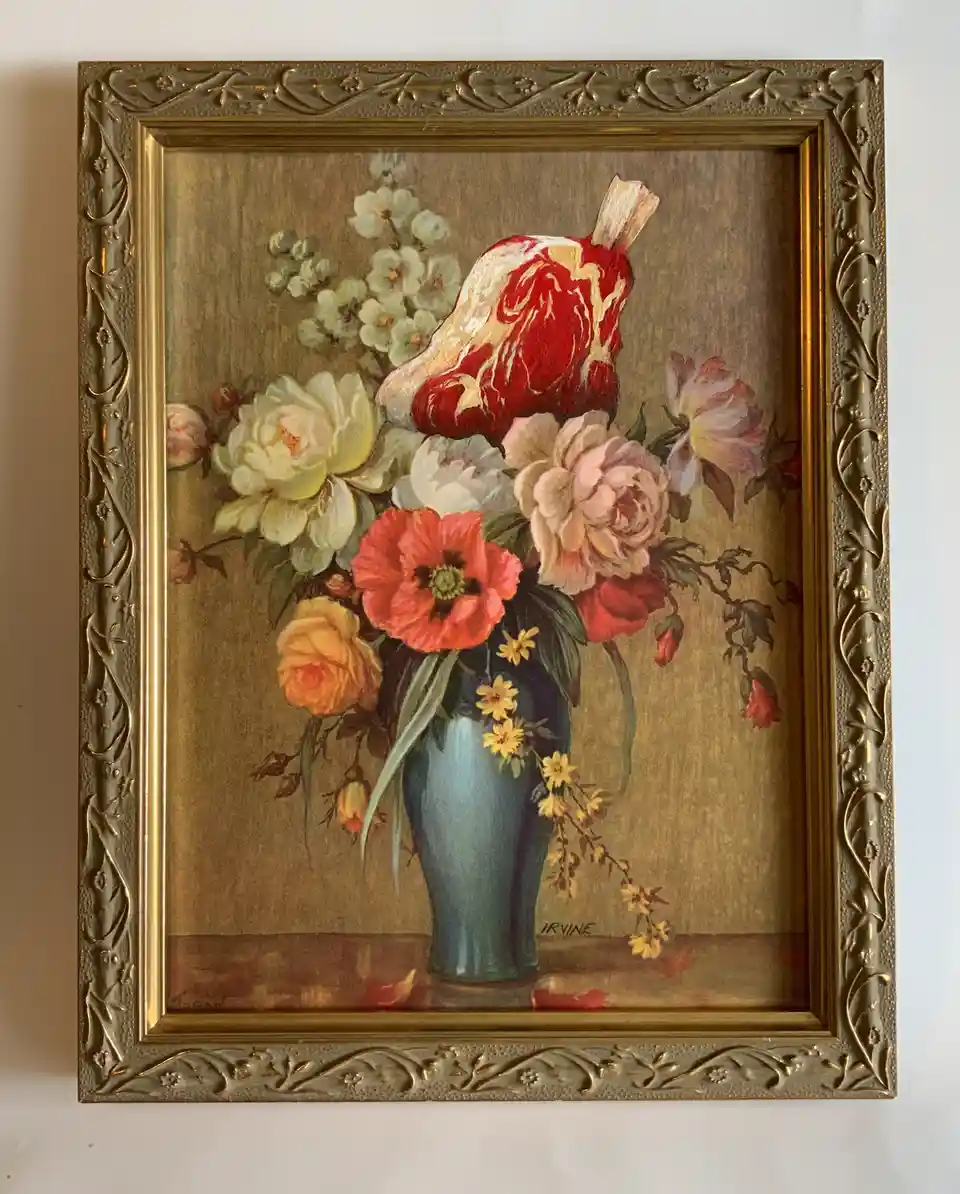 A framed painting depicts a bouquet of colorful flowers in a blue vase, but one prominent flower is replaced with a raw…