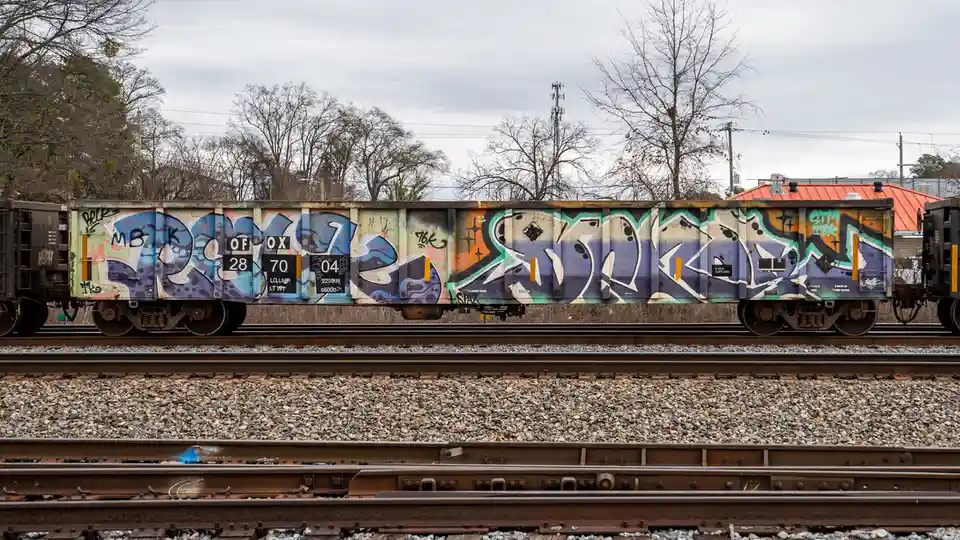 A side view of a graffiti-covered freight train car on railway tracks, with the word 'dope' spray-painted in large, stylized…