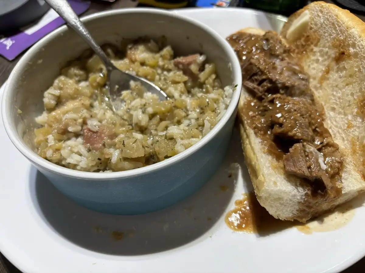 A close-up photo shows a white plate with a blue bowl of rice mixed with vegetables and meat, and a sandwich with shredded…