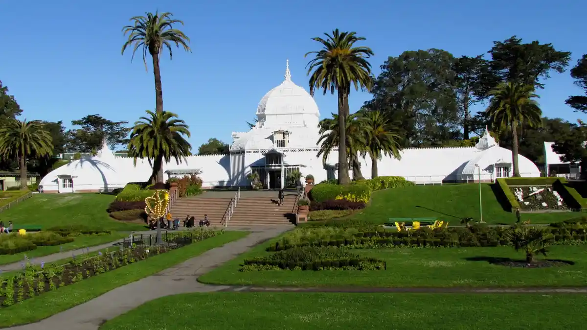 A wide shot of the Conservatory of Flowers in Golden Gate Park, San Francisco, showing its white glass and iron dome…