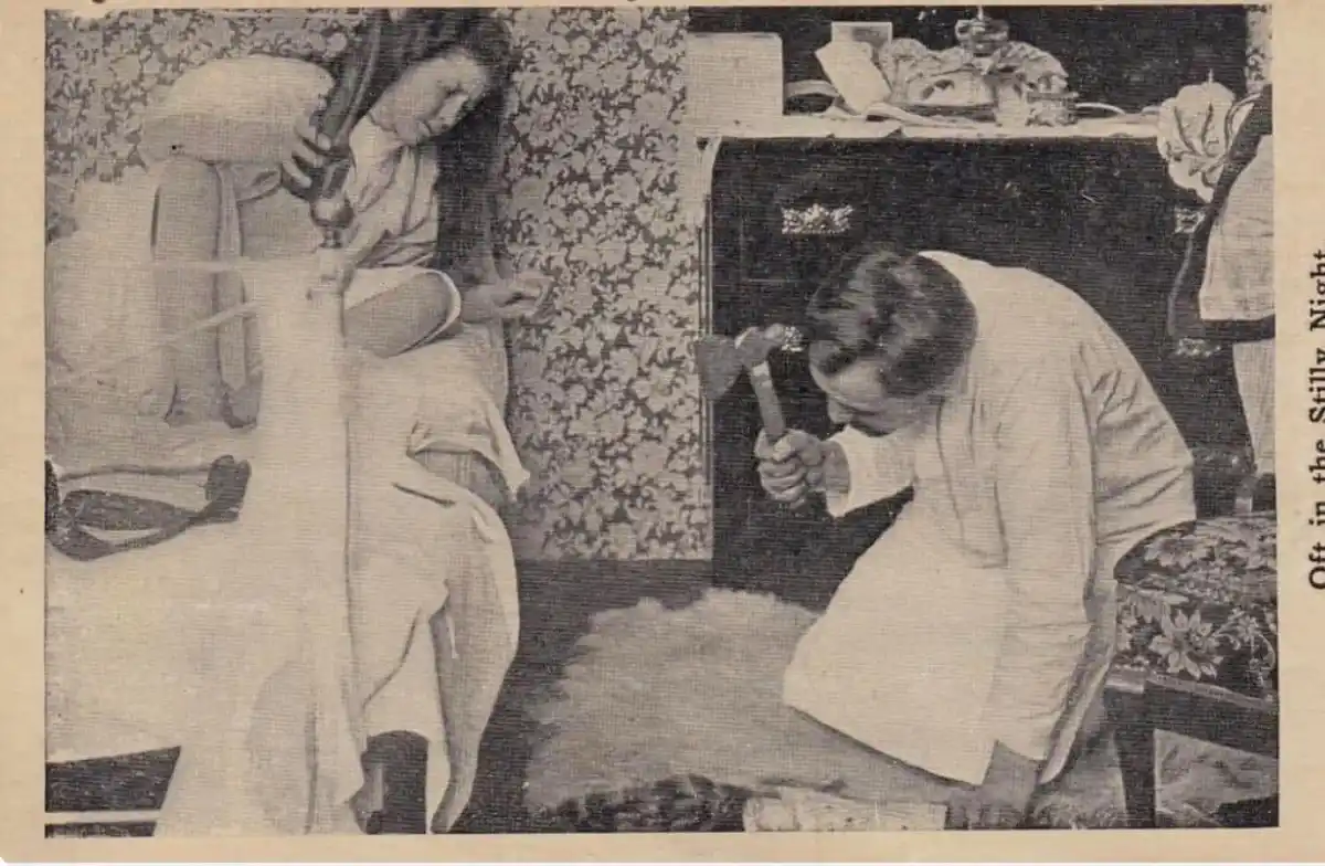A vintage black-and-white photo shows a woman in a robe sitting on a bed, looking down, while a man in a robe kneels on the…