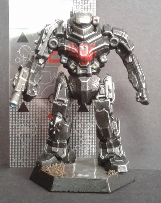 A painted miniature of a heavily armored, bipedal robot with glowing red eyes and a weapon, standing on a hexagonal base…