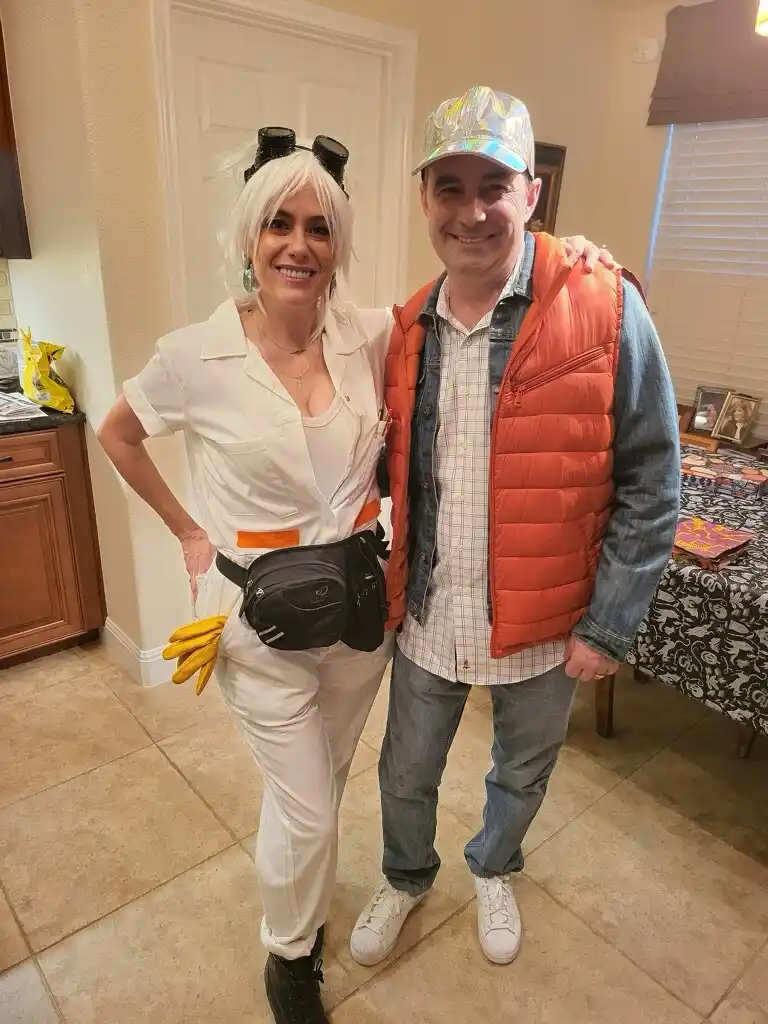 A man and woman pose indoors in costumes resembling characters from 'Back to the Future'. The woman wears a white jumpsuit…