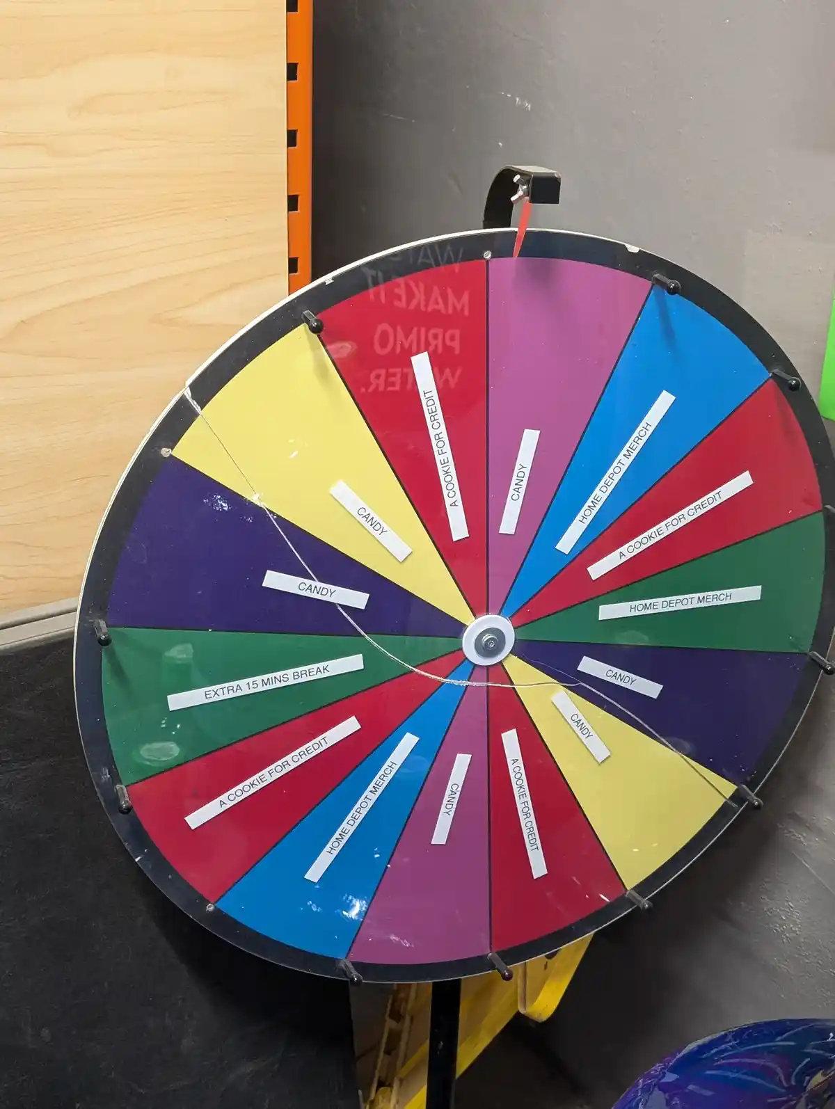 A colorful, multi-segmented prize wheel with a red pointer, mounted on a stand, has sections labeled 'CANDY', 'A COOKIE FOR…