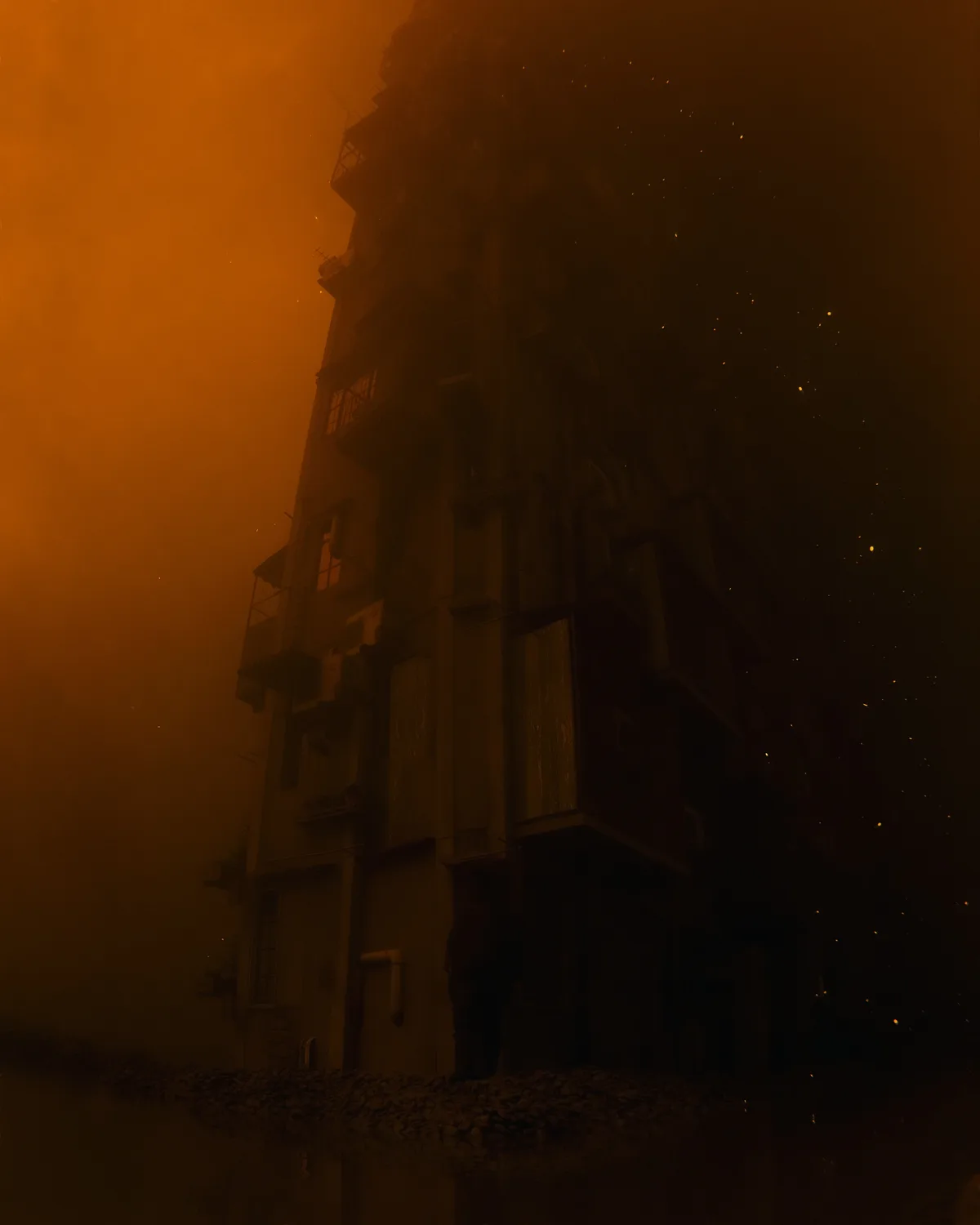 A dark, atmospheric image shows a tall apartment building silhouetted against an orange, smoke-filled sky with floating…