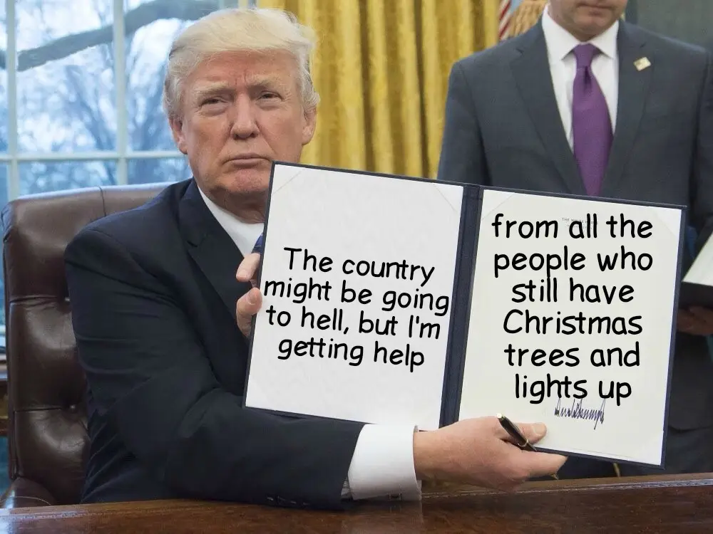A man in a dark suit sits at a desk holding up a binder with two pages of text. The left page reads 'The country might be…