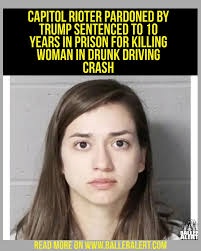 A mugshot-style photo of a young woman with long brown hair and a neutral expression, standing against a plain gray wall…