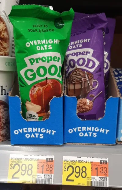 Two bags of 'proper GOOD' brand overnight oats, one green (apple flavor) and one purple (mocha flavor), are displayed in a…
