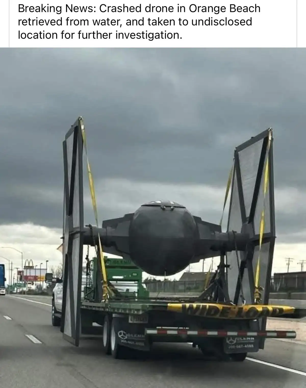 A large green flatbed truck with 'WIDE LOAD' markings is driving on a highway under a cloudy sky, hauling a full-sized…