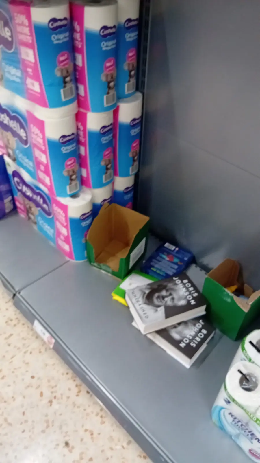 A blurry photo shows a supermarket shelf with stacks of toilet paper and two books titled 'Boris Johnson Unleashed' lying on…