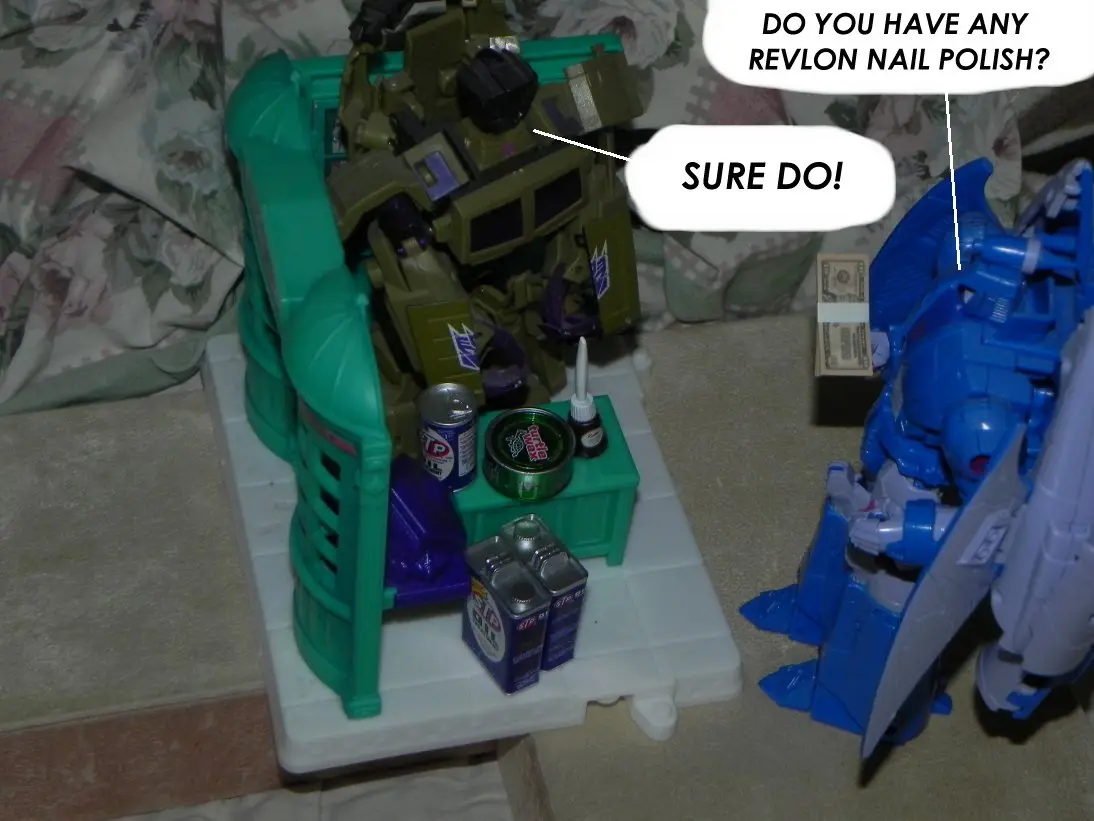 Two toy robots, one green and one blue, are shown in a room with a floral-patterned blanket in the background. The green…