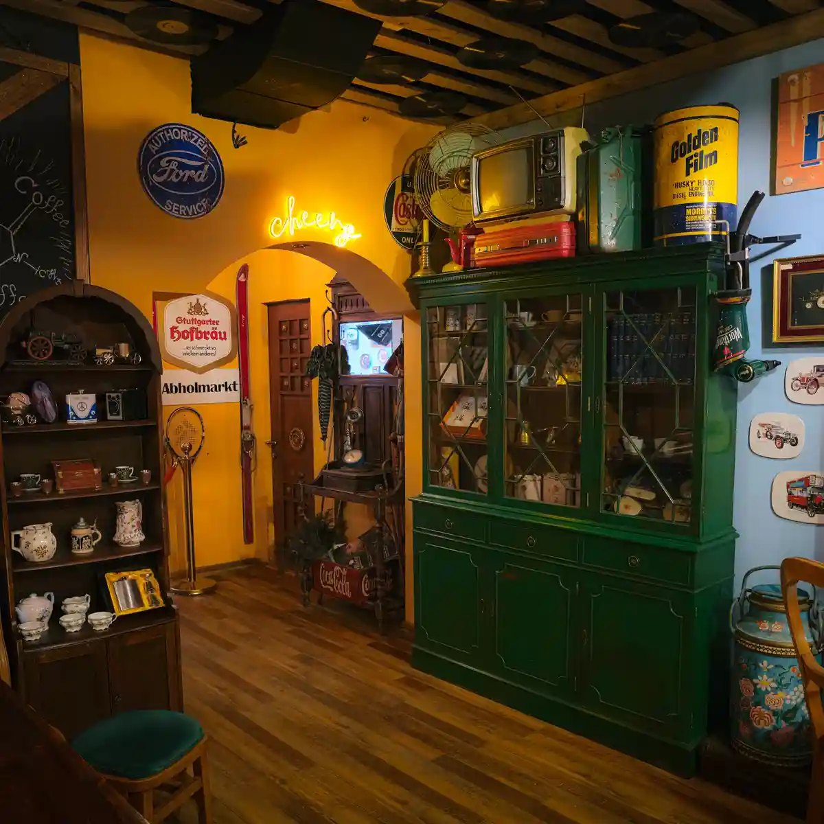 A warmly lit vintage-themed room filled with retro decor including a green china cabinet, an 'Authorized Ford Service' sign…