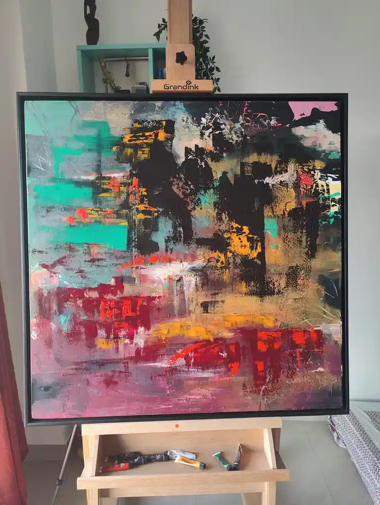 A large abstract painting with bold strokes of teal, black, orange, red, and pink sits on a wooden easel branded 'Grandink'…