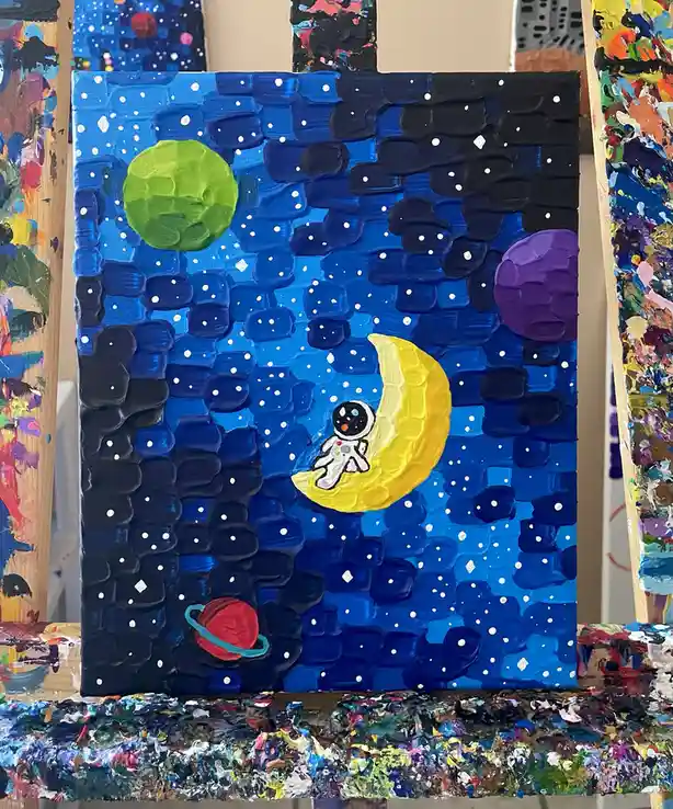 A textured, thickly painted canvas depicts a whimsical space scene with a cartoon astronaut sitting on a yellow crescent…