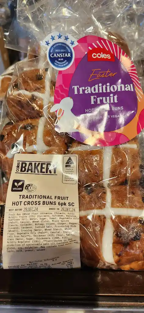 A close-up of a Coles brand package of traditional fruit hot cross buns, showing the colorful Easter-themed label and the…