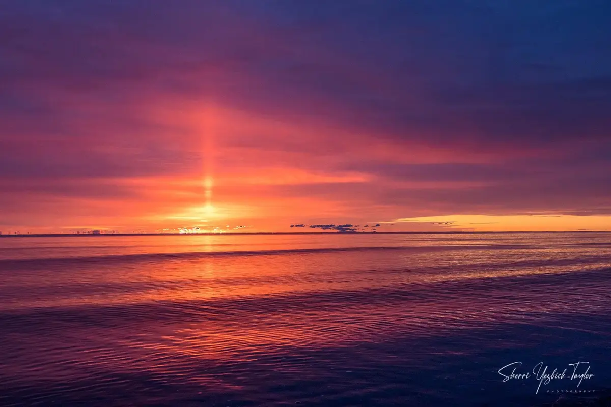 A serene sunset over a calm body of water, with vibrant orange and purple hues in the sky and a bright sun near the horizon…