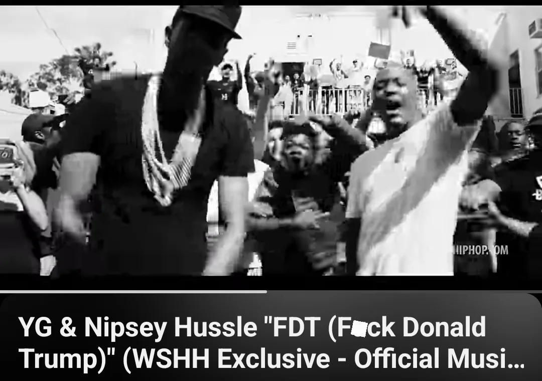 A black-and-white image shows two rappers, YG and Nipsey Hussle, performing energetically in front of a crowd. The crowd is…