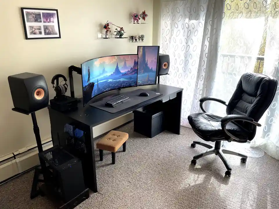 A well-lit room features a black desk with a curved and a vertical monitor displaying fantasy landscapes, flanked by large…