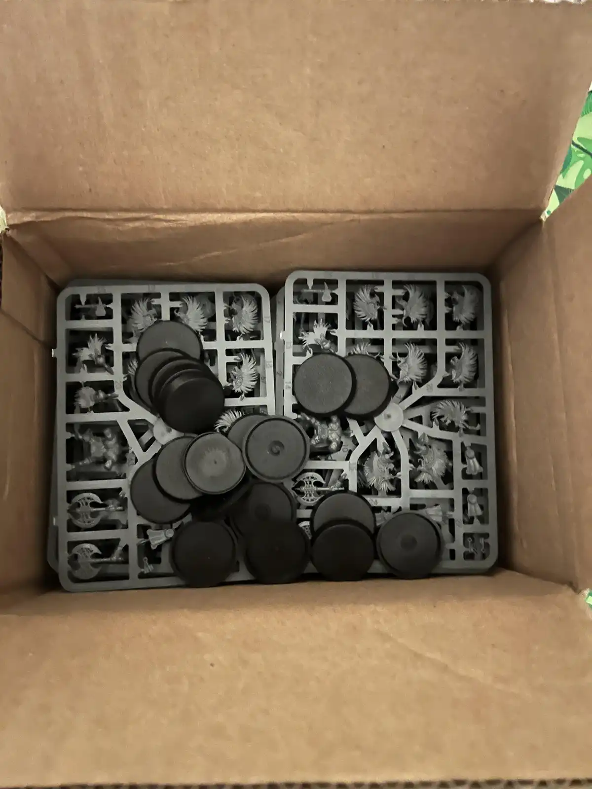 An overhead shot shows two grey plastic sprue sheets with unpainted fantasy miniatures still attached, partially obscured by…