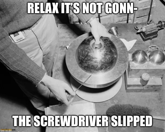A black and white photo shows a person in a sweater and pants using a screwdriver on a large, round, metallic object. The…