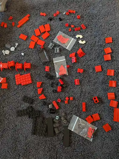 A top-down view of scattered red, black, and white Lego pieces arranged on a gray carpet, with some pieces forming the…