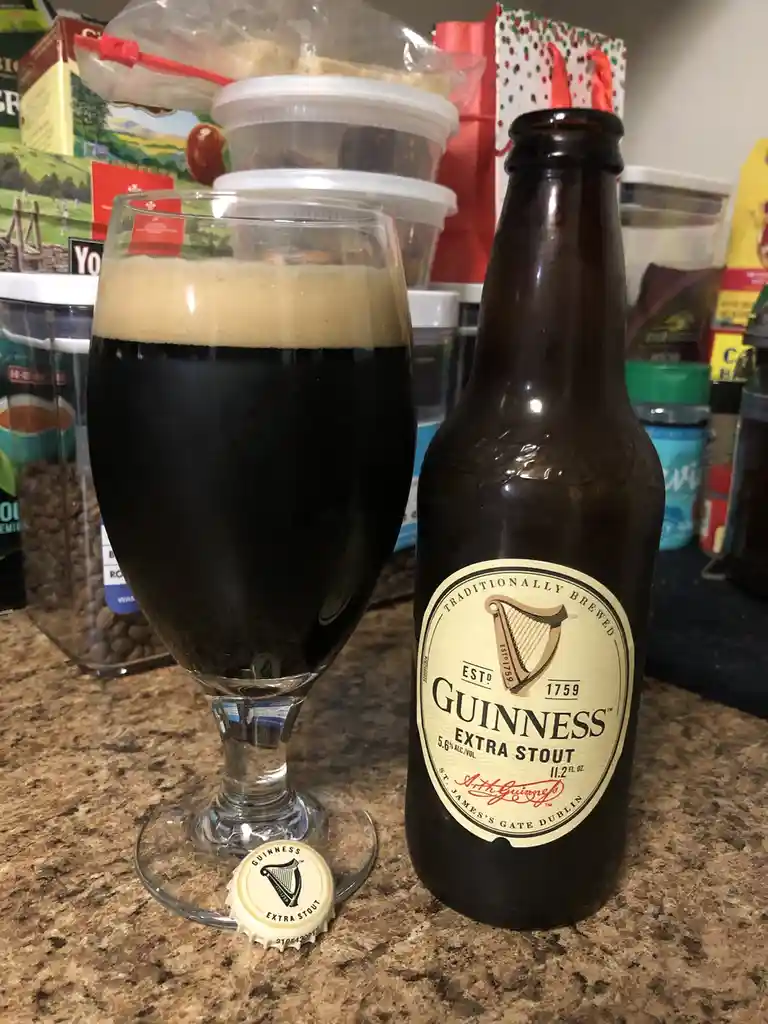 A bottle of Guinness Extra Stout and a glass filled with the dark beer, topped with a creamy head, sit on a kitchen counter…