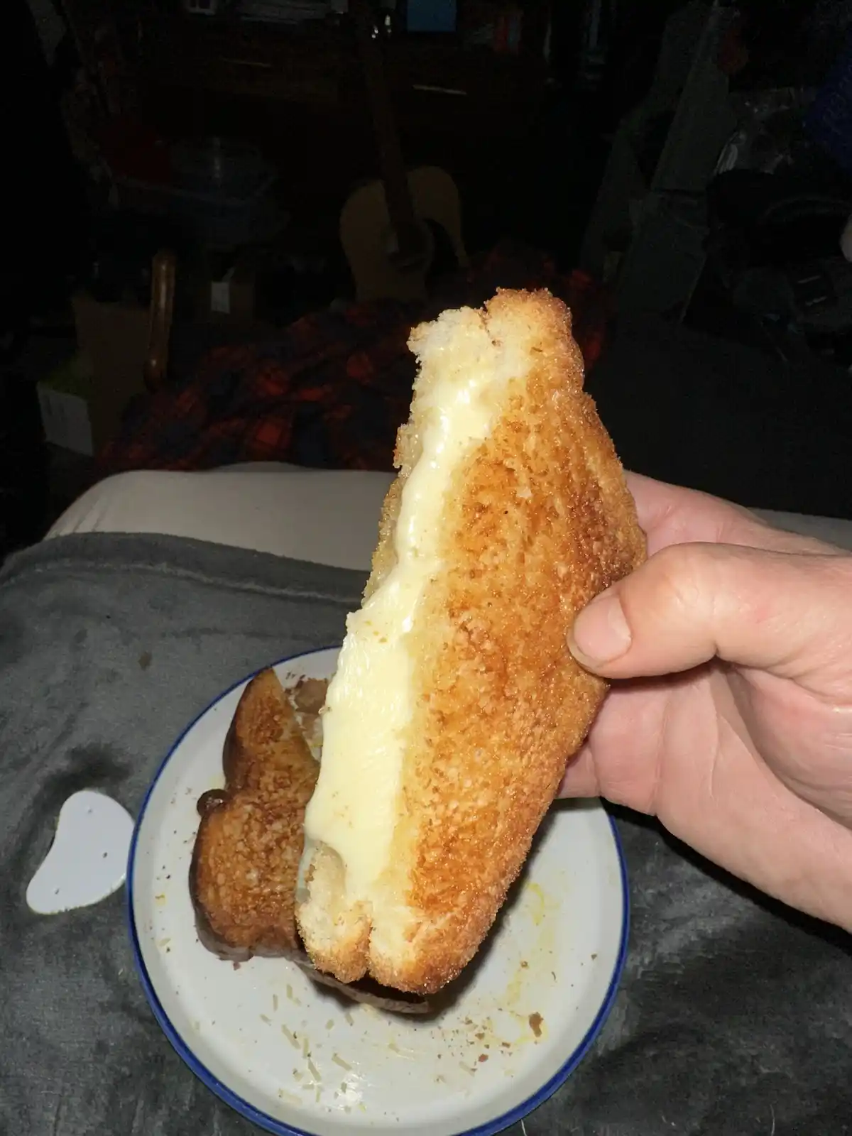 A hand holds up a half-eaten grilled cheese sandwich, showcasing its melted, oozing cheese. The sandwich sits on a white…