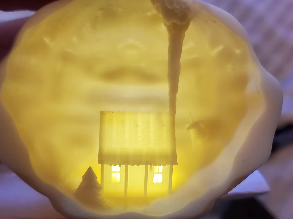 A close-up of a yellow, translucent, squishy object resembling a melted candle or gelatin dessert, with a small house and…