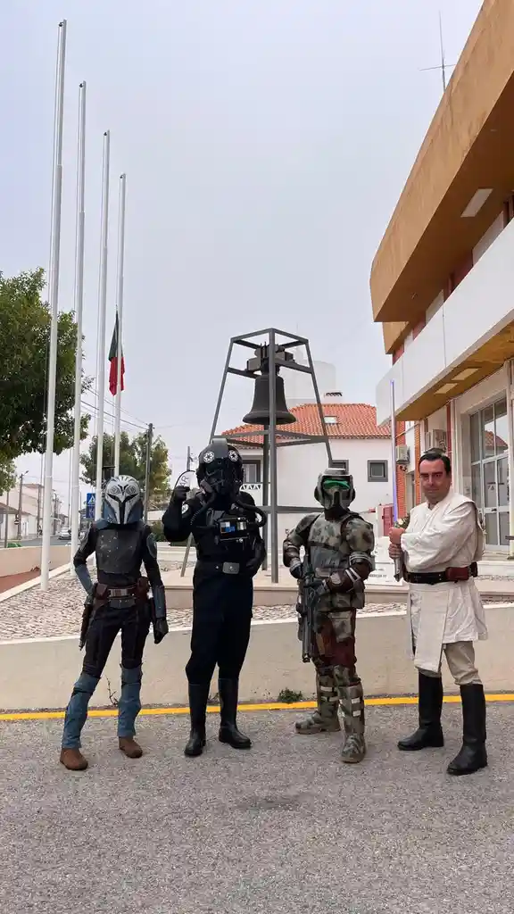 Four people dressed as Star Wars characters — a Mandalorian, a Stormtrooper, a Clone Trooper, and a Jedi — stand in a public…