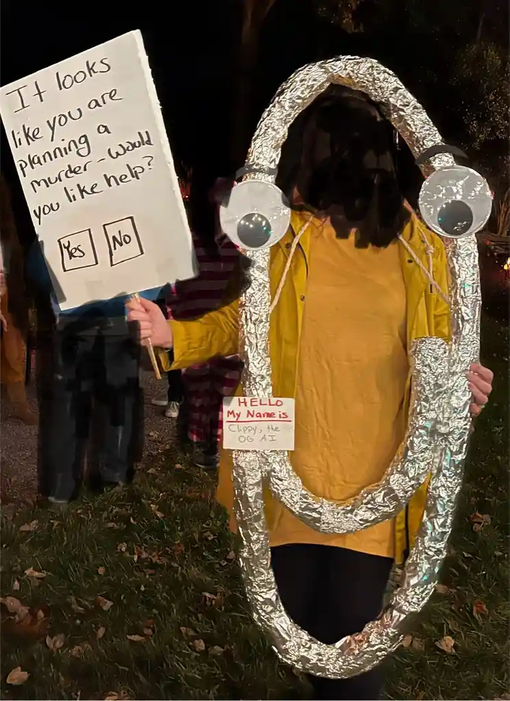 A person in a homemade costume made of aluminum foil shaped like a large, smiling mouth with googly eyes, wearing a yellow…