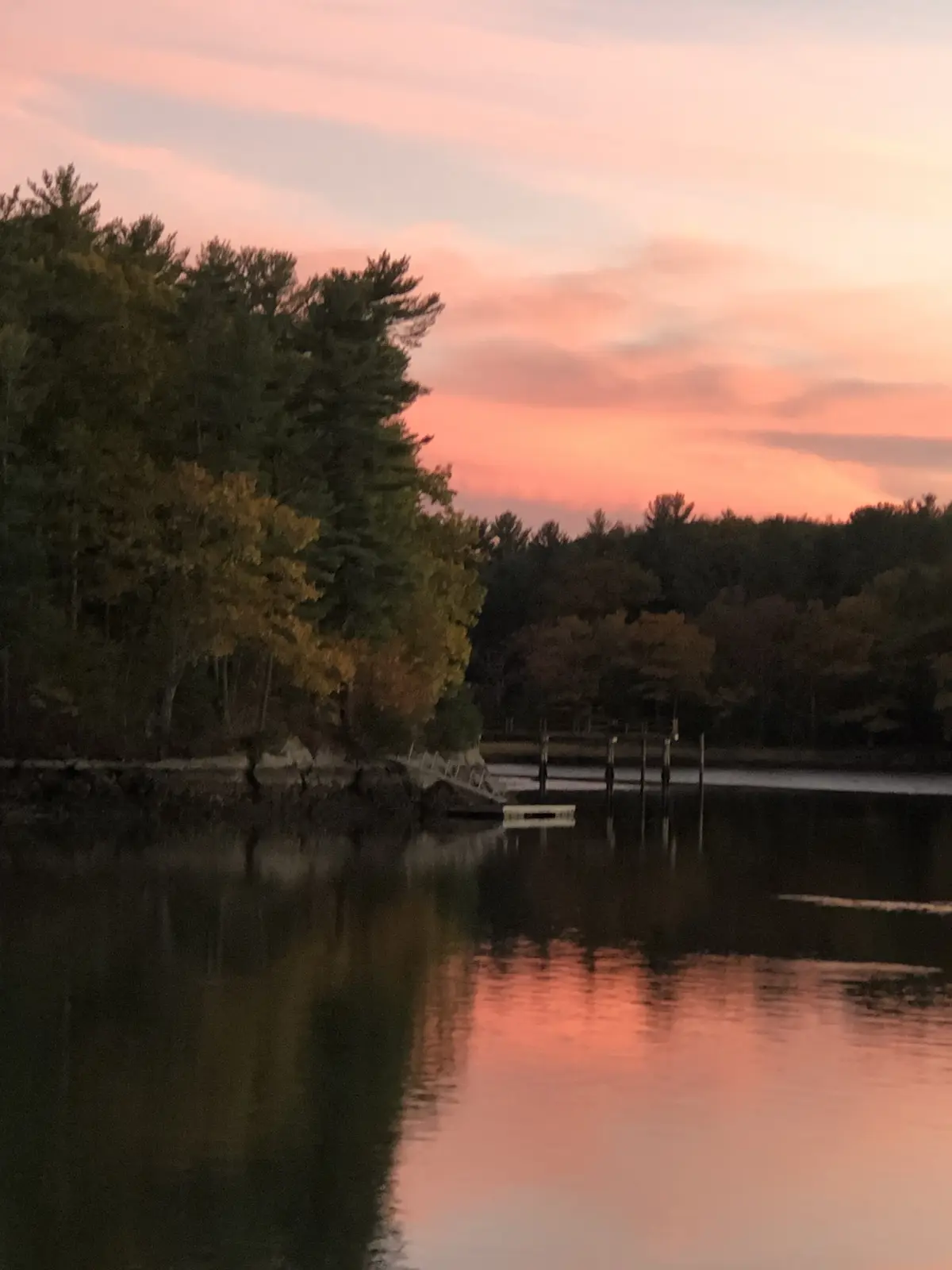 A serene sunset over a calm lake with trees lining the shore, their reflections shimmering in the water. The sky is painted…