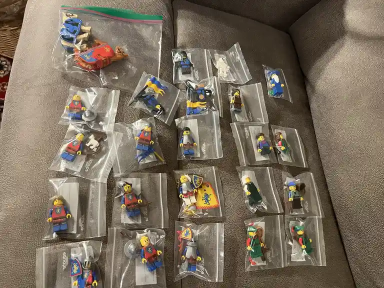 An overhead shot shows dozens of Lego minifigures, mostly from the 'Ninjago' or 'Castle' themes, individually sealed in…