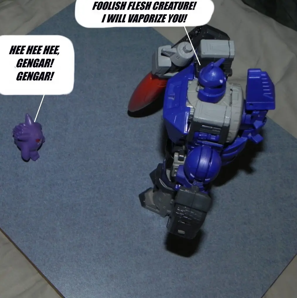 A small purple Gengar toy figure laughs maniacally while facing a large blue and gray robot toy, which responds with a…