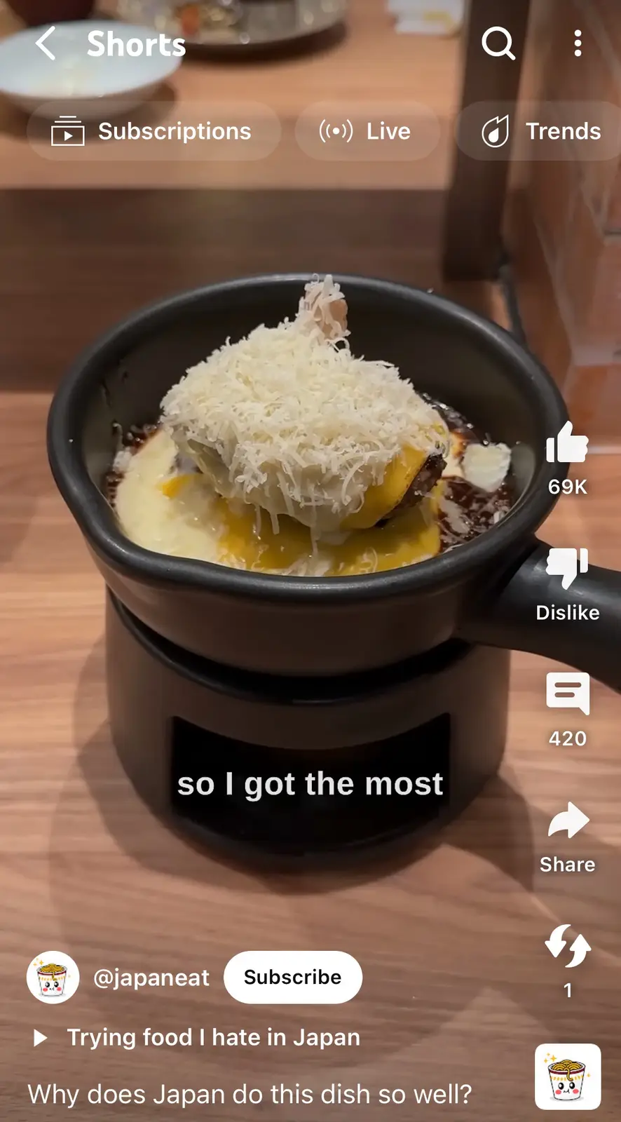 A close-up shot of a small black pot on a warmer, filled with a dish topped with a large mound of shredded white cheese…